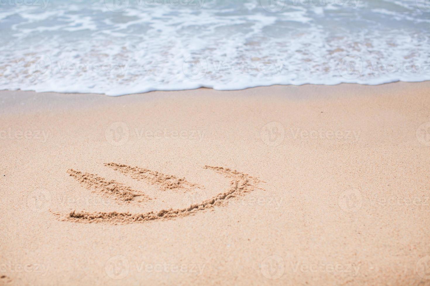 Happy smile drawing on the sand at tropical beach photo