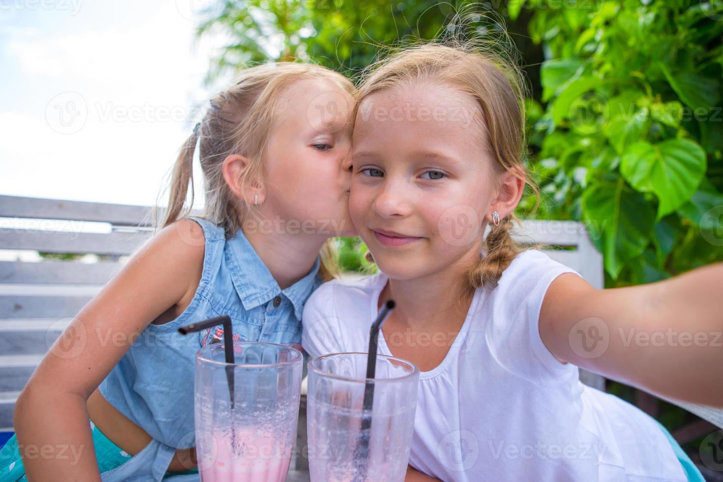 niñas pequeñas tomando selfie y bebiendo sabrosos cócteles en un café al aire libre foto
