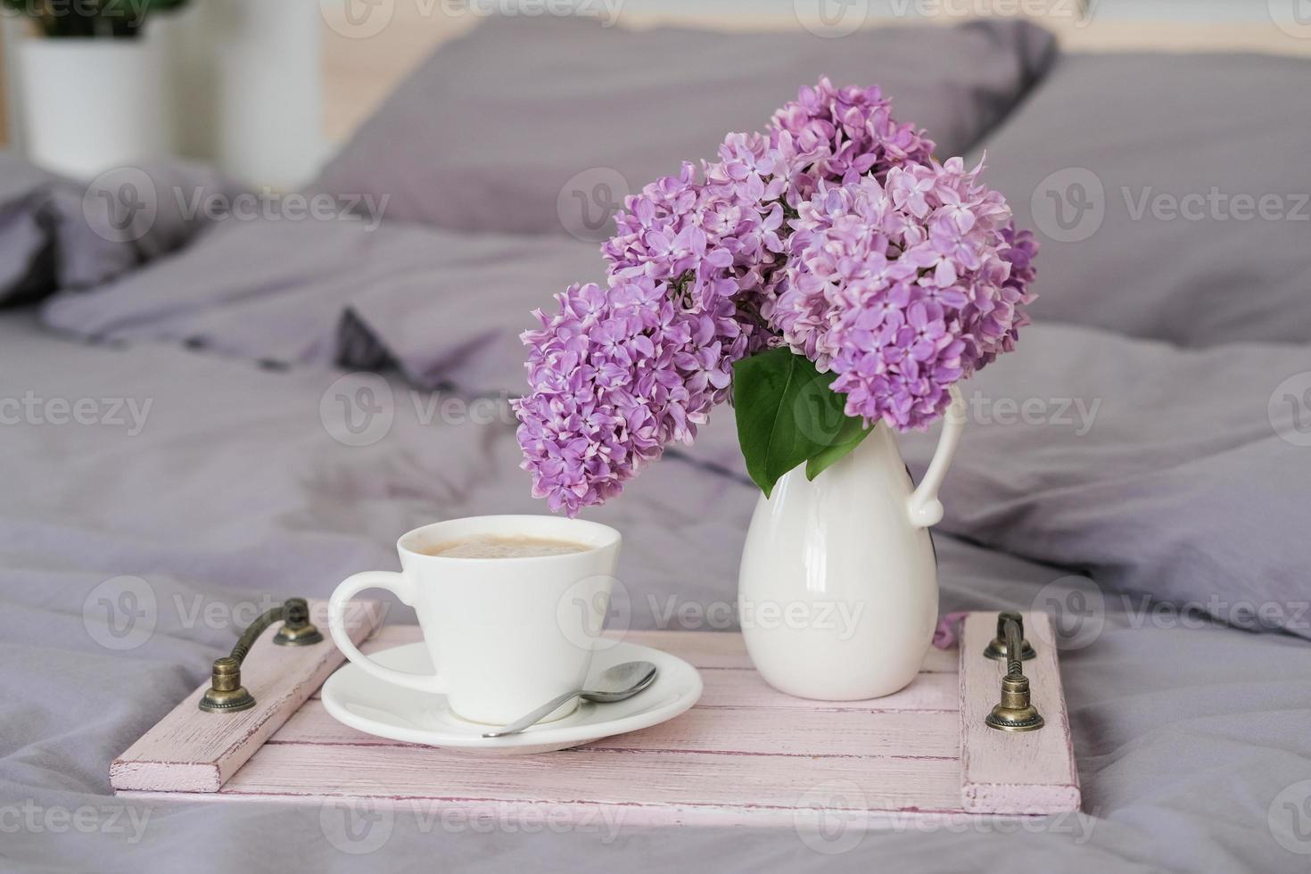 Breakfast in bed. Tray with coffee and a bouquet of lilacs on the bed in the bedroom photo