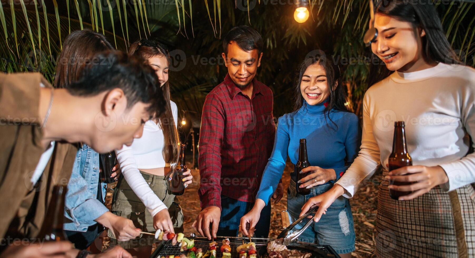 Happy Asian friends cheering with barbecue dinner outdoor - Group of people having fun in new year party. People, food and drink lifestyle concept Night Party, people and celebration concept. photo