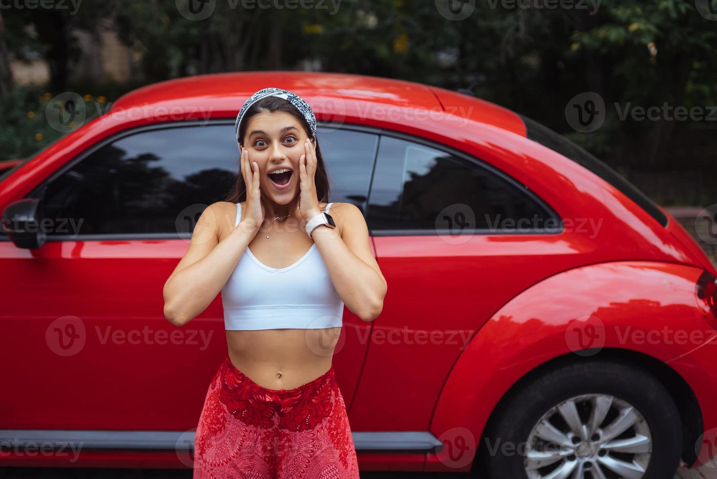 Portrait of pretty Caucasian woman standing against new red car photo