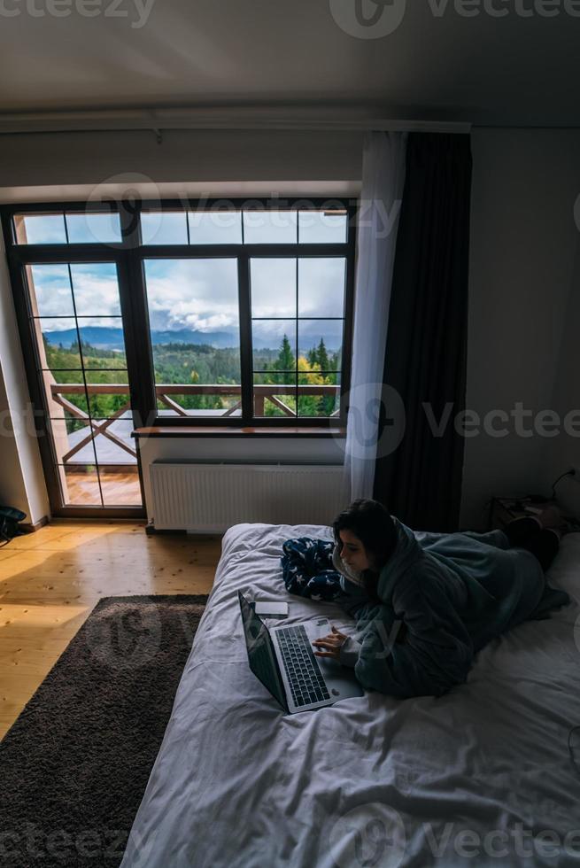 Young woman working on laptop while lying on bed photo