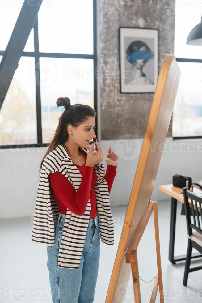 Young woman applies makeup on her face in front of the mirror photo