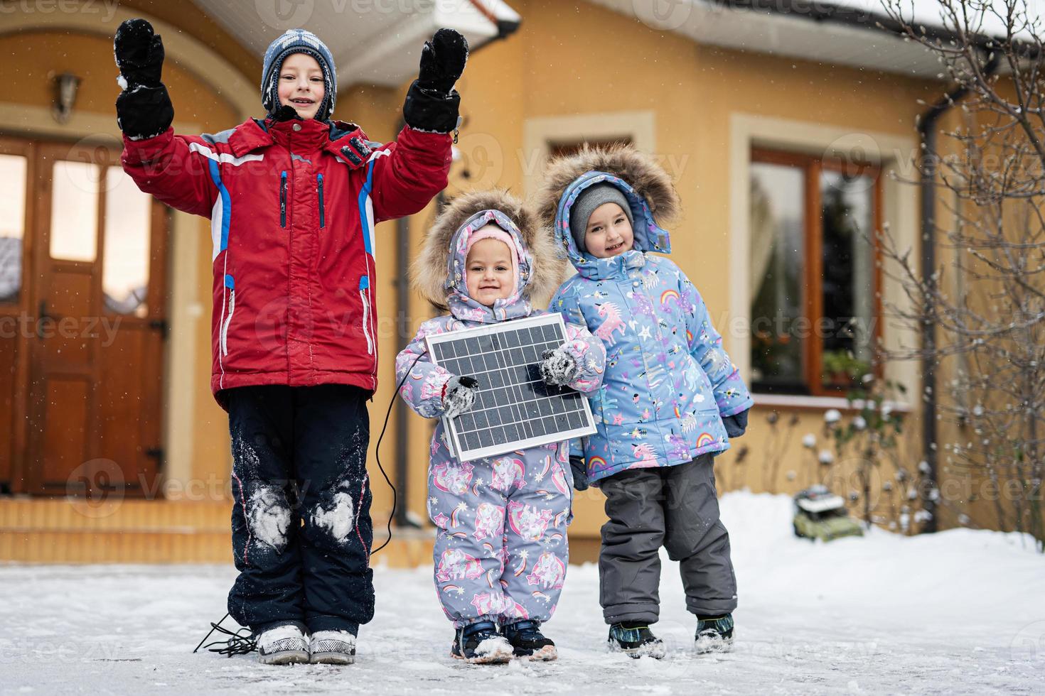 Kids with solar panel against house in winter. Alternative energy concept. photo