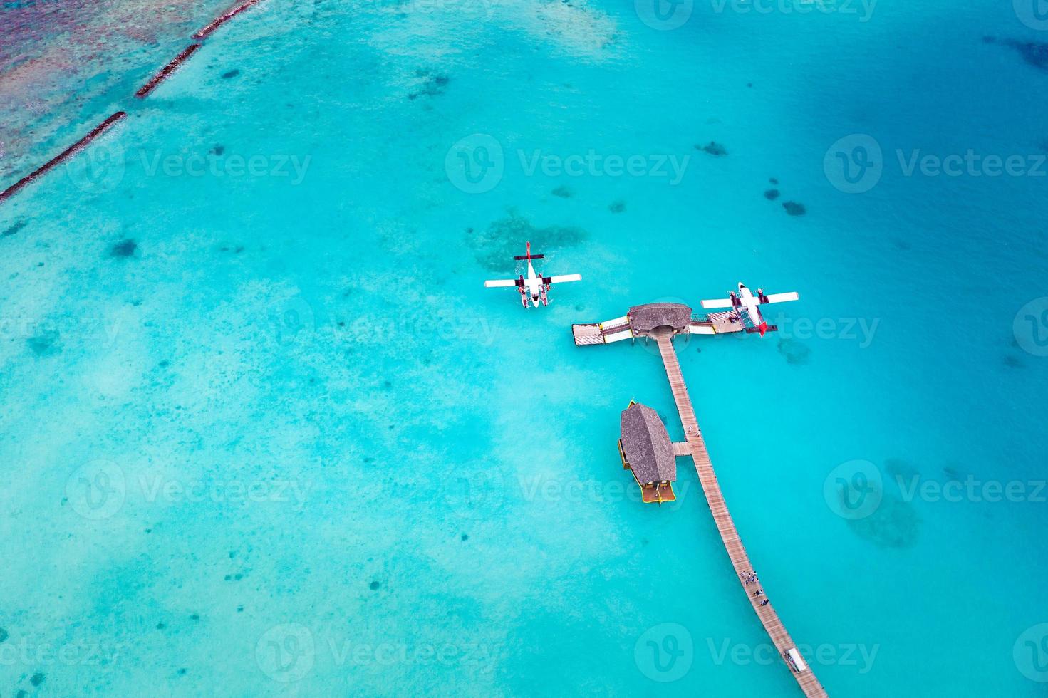 Beautiful aerial view of Maldives jetty seaplane top view with wooden boat and tropical beach. Luxury tropical resort or hotel with water villas and beautiful beach scenery. Amazing bird eyes view photo