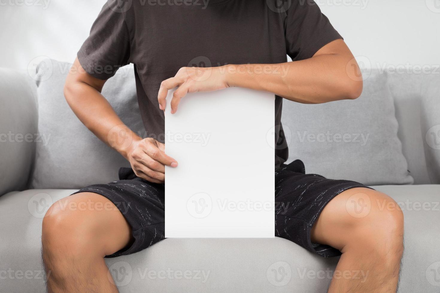 A man holding a white paper sitting on a gray sofa. photo