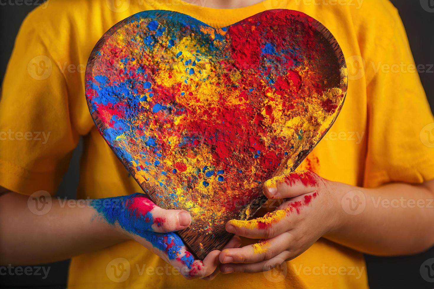 children's hands hold a wooden plate in the shape of a heart in which the multi-colored bright colors of Holi. photo