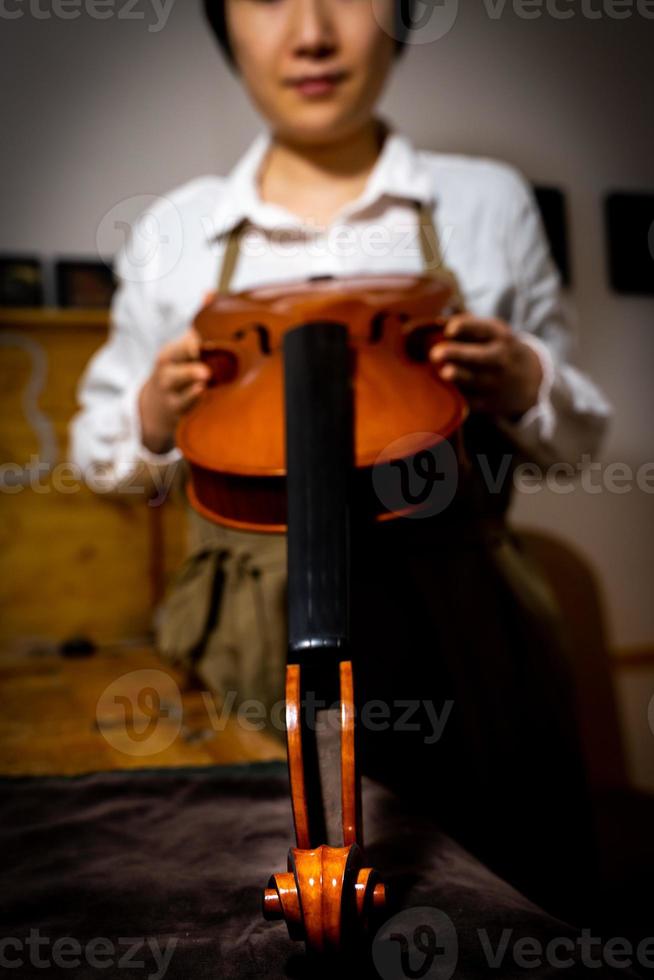 young chinese woman violin maker checking the quality of her violin in the workshop photo