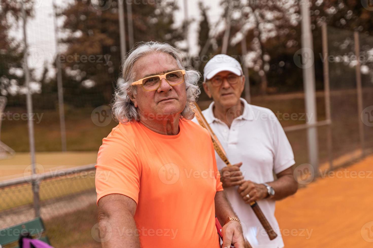 portrait of two senior tennis players dressed in sportswear relaxing at the end of the game on a clay tennis court photo