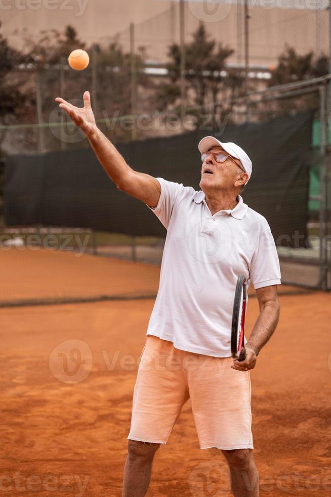 tenista senior vestido con ropa deportiva en acción en una cancha de tenis de tierra batida foto