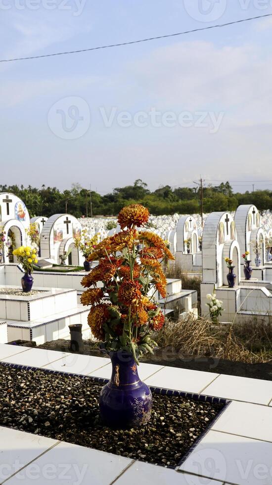 Tombstone and flowers in a vase on a white ceramic grave in cemetery or graveyard. photo