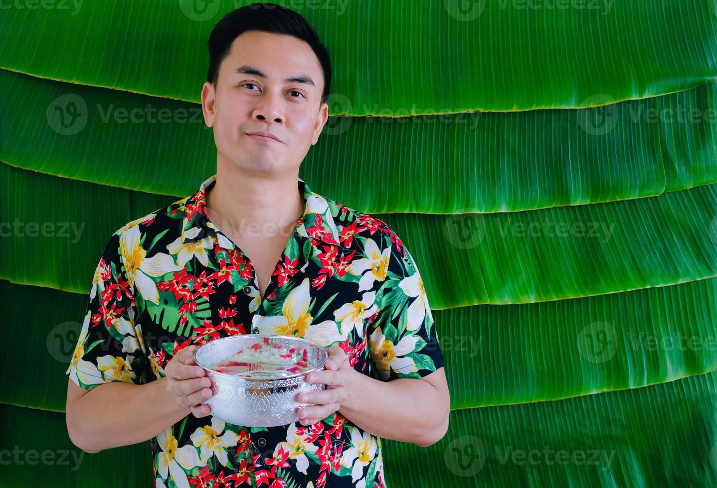 Thai man holding water bowl that have flowers to give blessing for Songkran festival with banana leaf background. photo