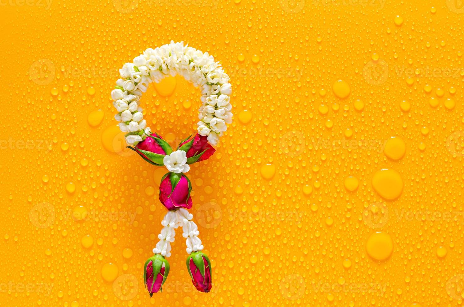 Jasmine garland puts on clear mirror that have wet yellow background below for Songkran festival concept. photo