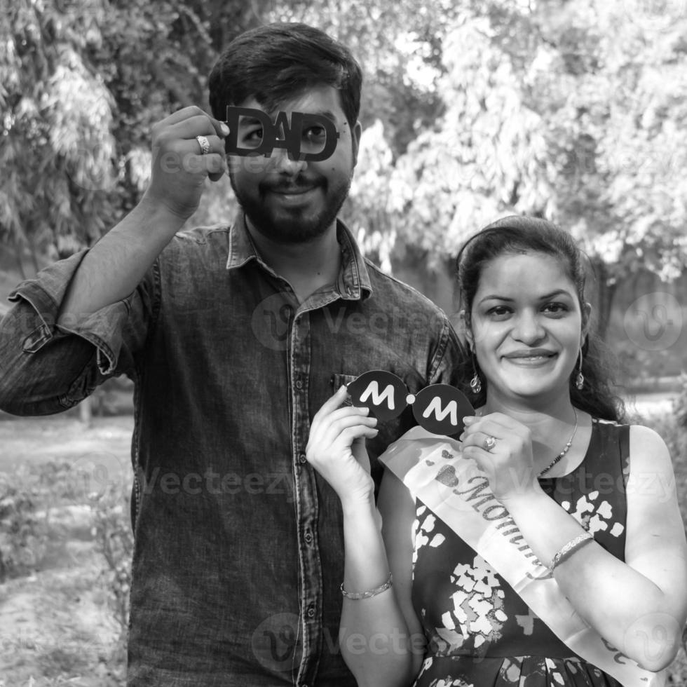 Indian couple posing for maternity baby shoot. The couple is posing in a lawn with green grass and the woman is falunting her baby bump in Lodhi Garden in New Delhi, India - Black and White photo