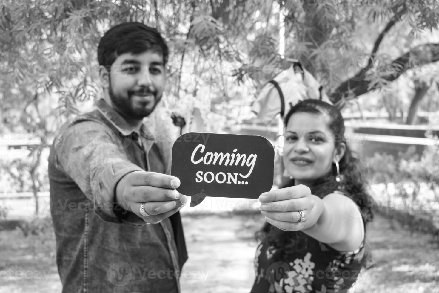 Indian couple posing for maternity baby shoot. The couple is posing in a lawn with green grass and the woman is falunting her baby bump in Lodhi Garden in New Delhi, India - Black and White photo