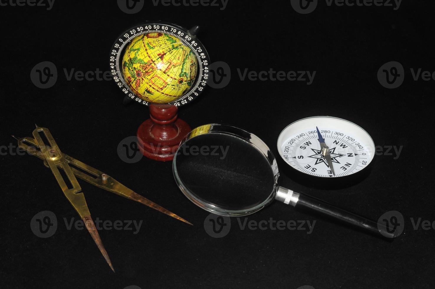 Compass, globe and magnifying glass on black background photo