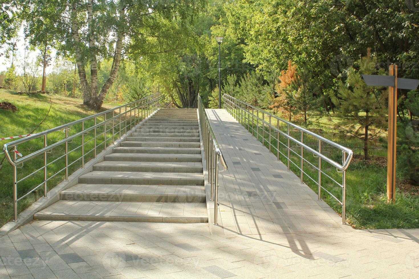 Stairs and ramp with metal railings for the passage of strollers and wheelchairs in public park. Concept of comfortable barrier-free urban environment in city. Pathway for people with disabilities photo