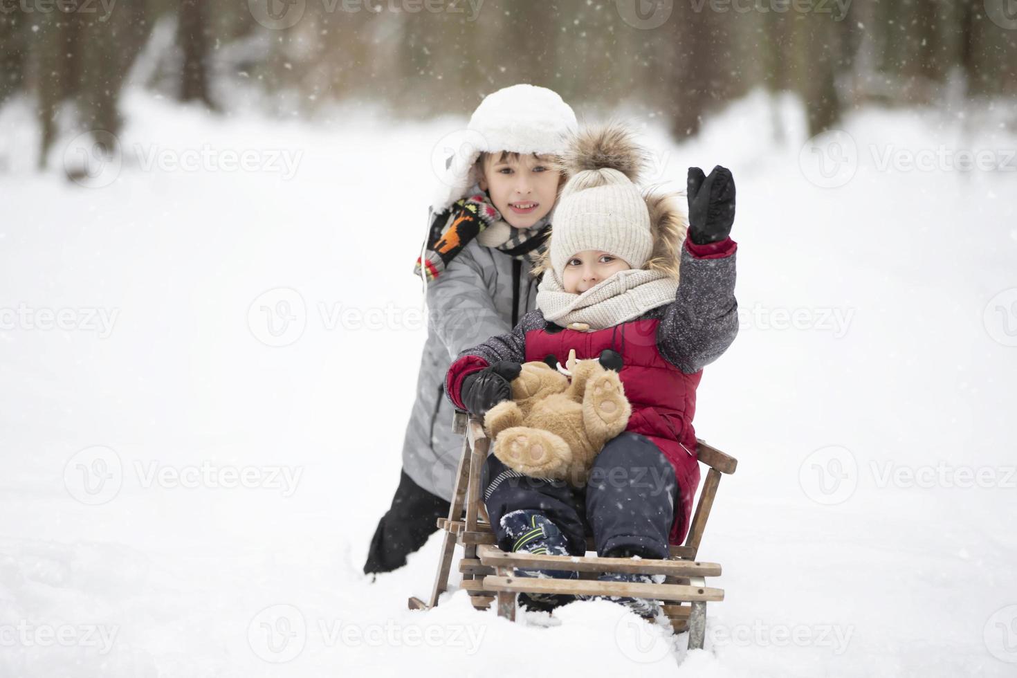Two brothers ride on a vintage wooden sled against the backdrop of a winter forest. photo