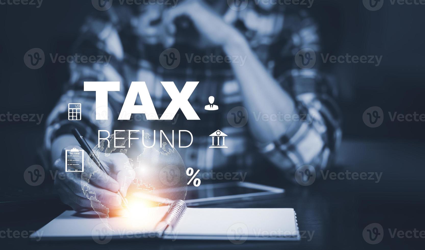 Businessman using a pen to write a notebook with TAX REFUND and refund tax of duty taxation business, graphs and chart being demonstrated on the screen media,  tablet pc and selecting tax refund. photo