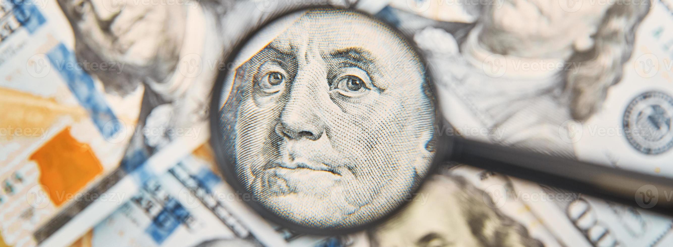 Magnifying glass on a pile of 100 dollar banknotes photo