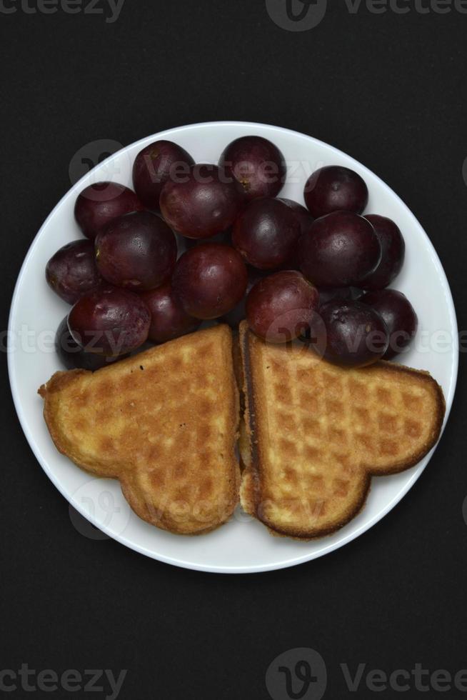 Delicious waffles and grapes on a plate. A sweet breakfast of waffles and red grapes. Heart-shaped waffles. photo