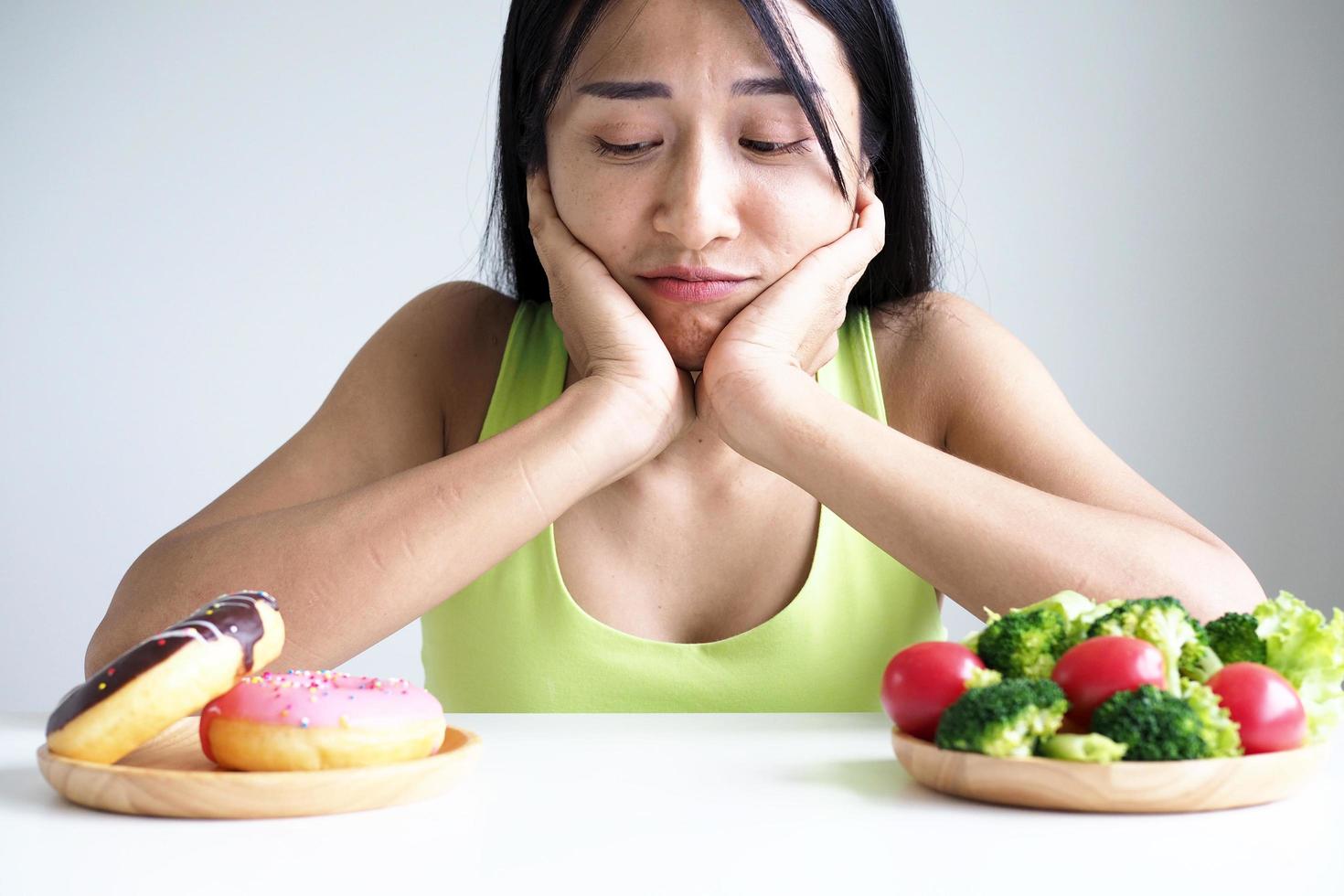 hermosas mujeres asiáticas eligen entre verduras y donuts. perder peso foto