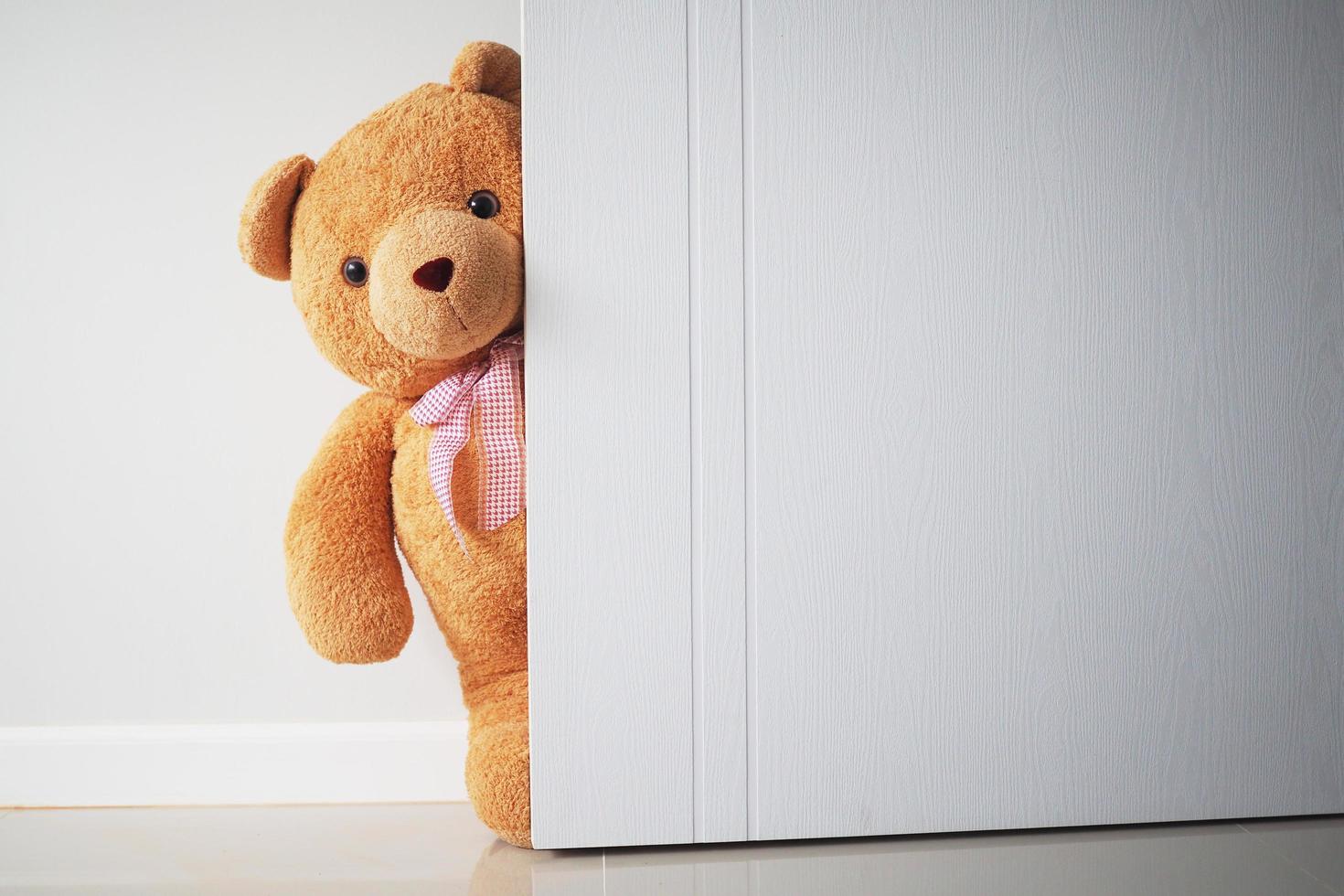 oso de peluche con cabello castaño detrás de la puerta abierta. fondo para niños jugar oso de peluche foto