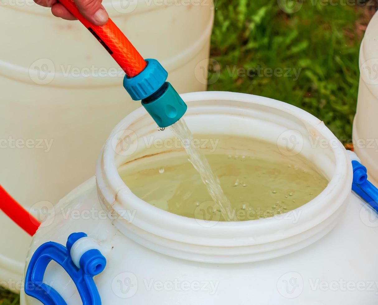 A woman's hand fills a plastic barrel with water from a hose. The concept of the drinking water crisis in the world. photo