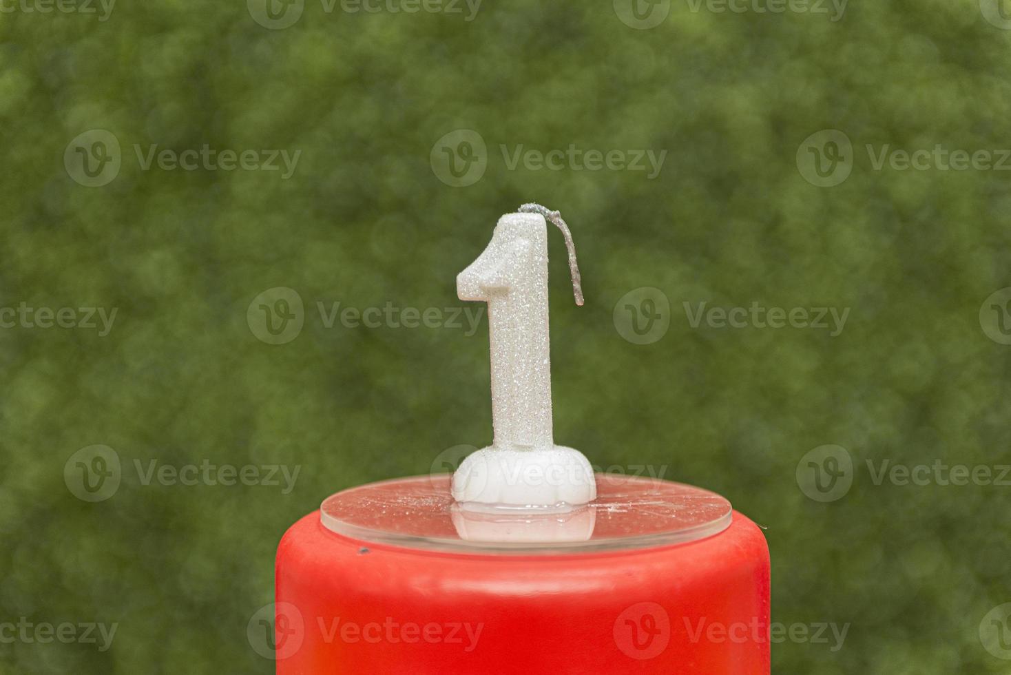 top of red fake cake with one-shaped candle with blurred green background. photo
