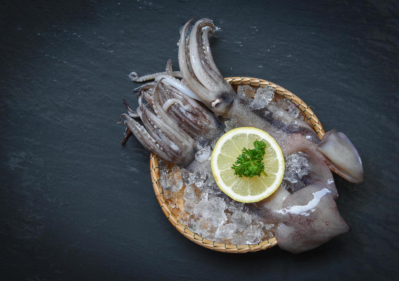 Seafood fresh squid on ice in basket with lemon parsley on dark background photo