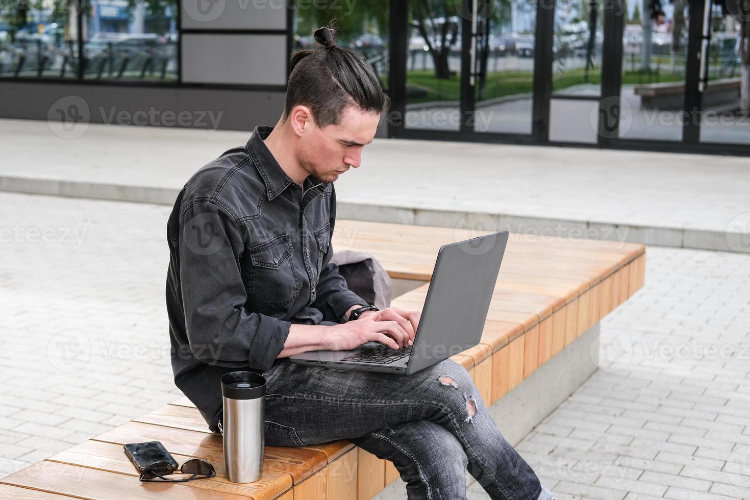 A young freelancer is working on a laptop in the city. Online business, freelance, remote work. Training and education photo