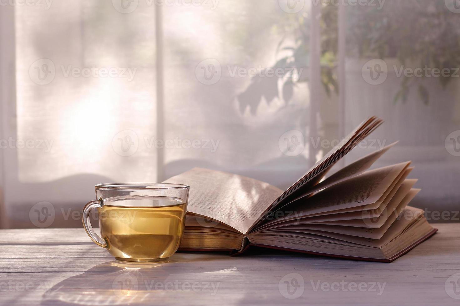 A cup of green tea, an open book on a white wooden table by the window in the sunlight. photo