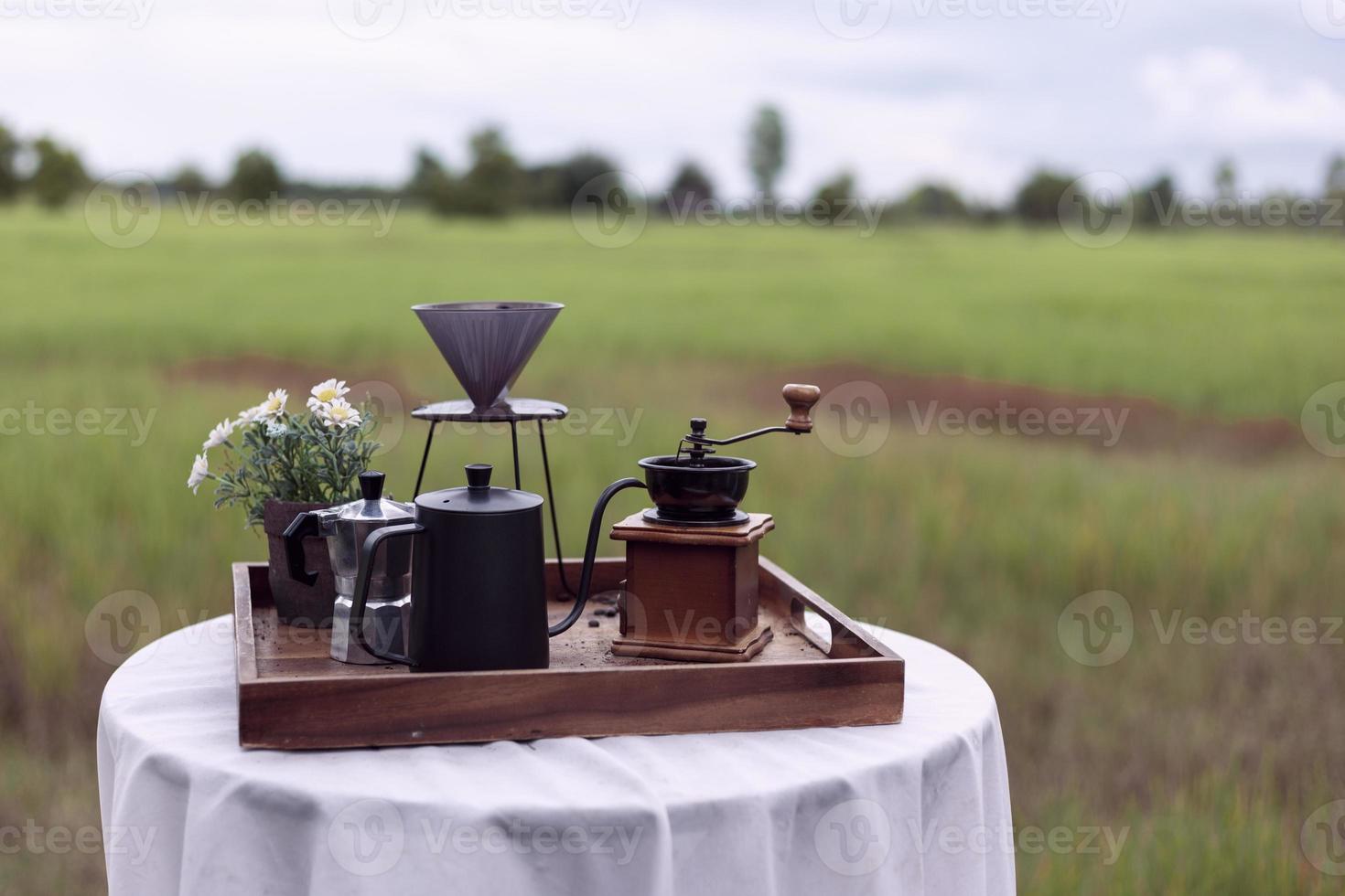 Old-fashioned coffee-making equipment is placed on a table covered with white cloth and the rice field atmosphere gives a nostalgic feel to traditional coffee brewing. photo