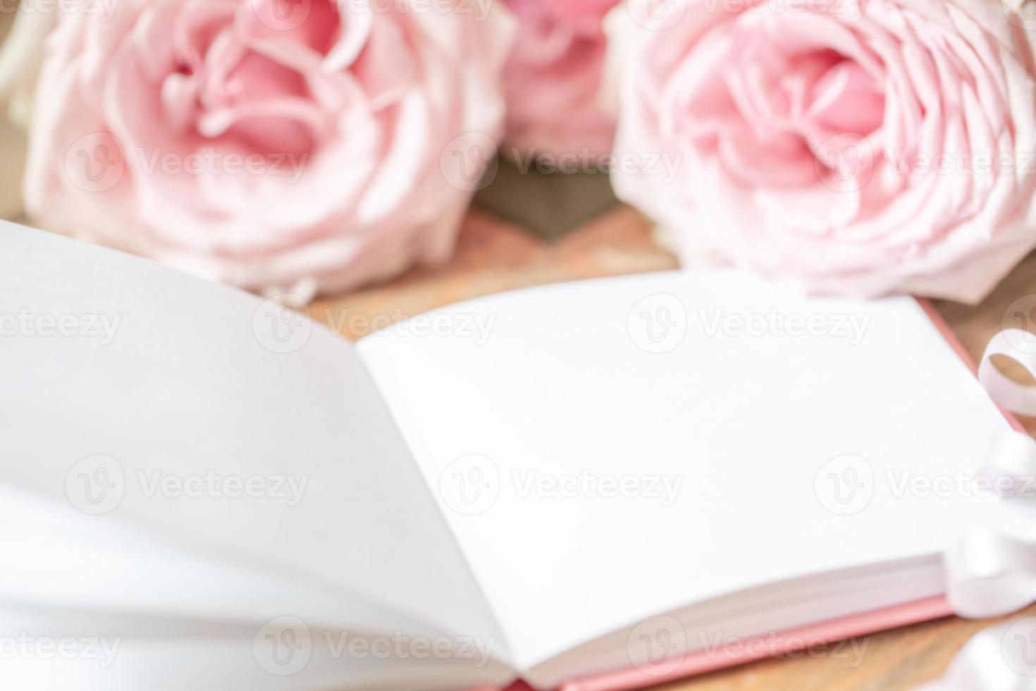 Gentle pale pink roses and open white empty blank notepad close up. Festive blur image for text. photo