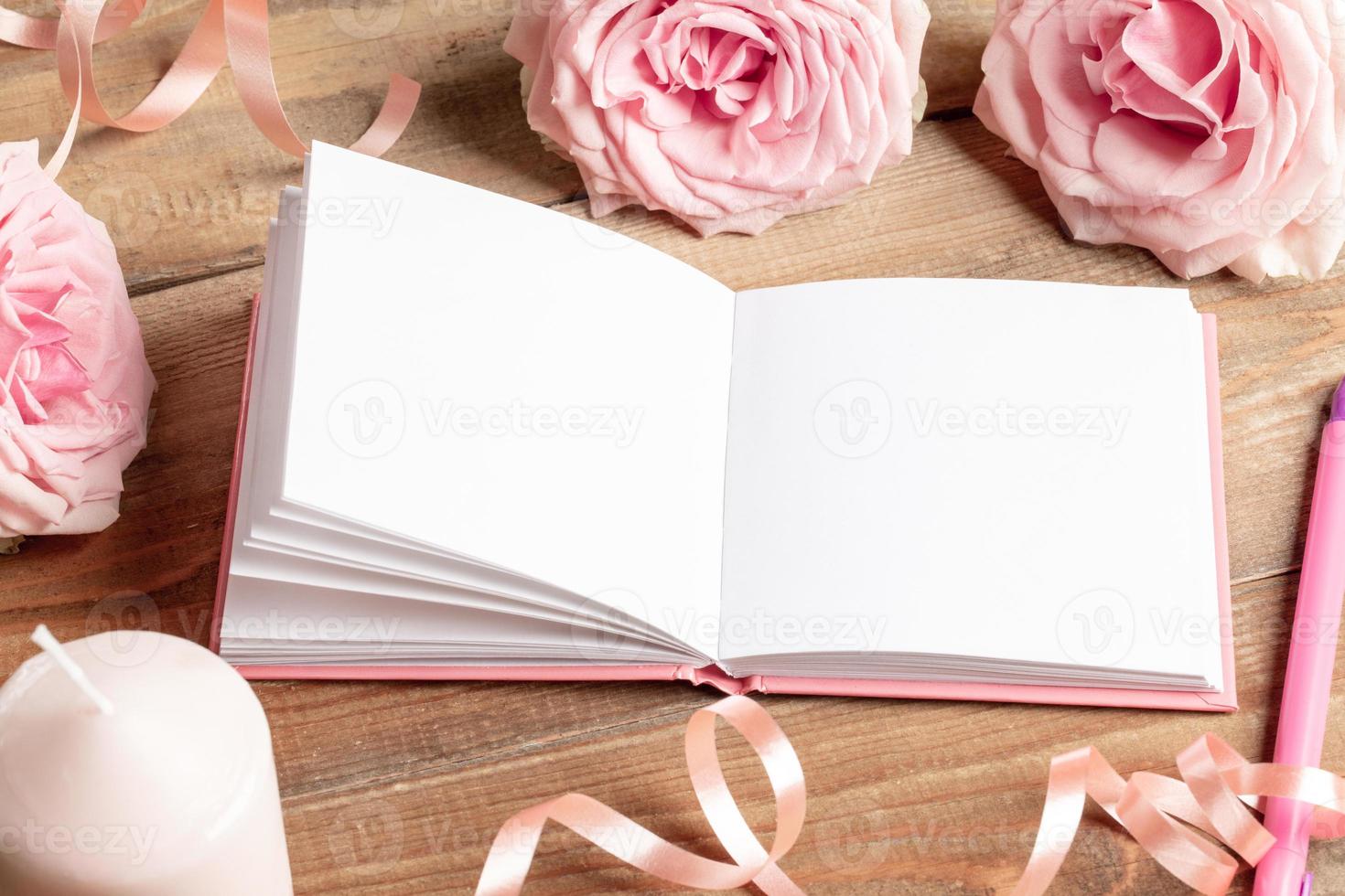 Opened white empty blank notepad, gentle, pink roses, candle, pen, ribbon on old wooden table. photo