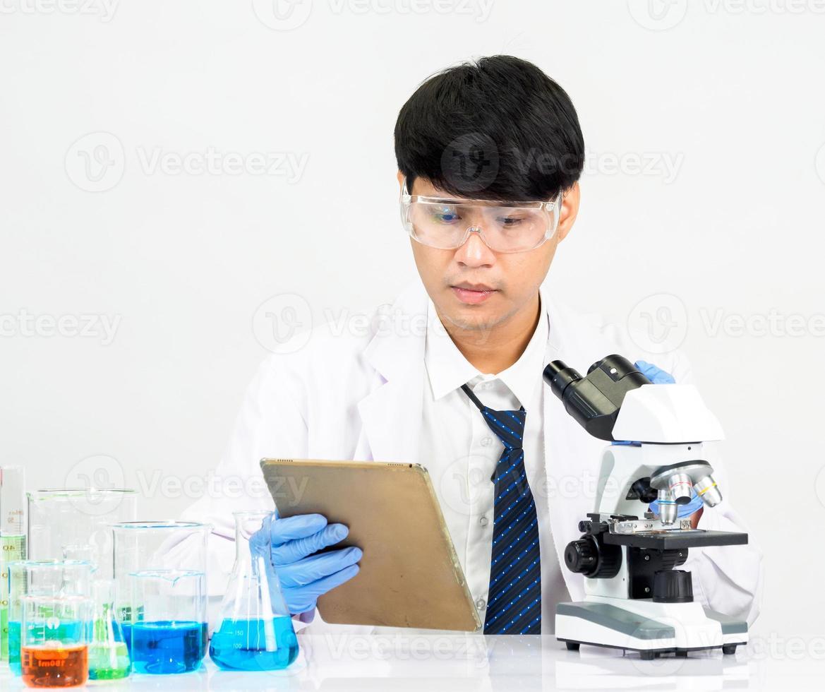 estudiante científico asiático en un laboratorio de mezcla de reactivos en un laboratorio de investigación científica con tubos de ensayo de varios tamaños y microscopios. sobre la mesa en el fondo blanco de laboratorio de química de laboratorio. foto