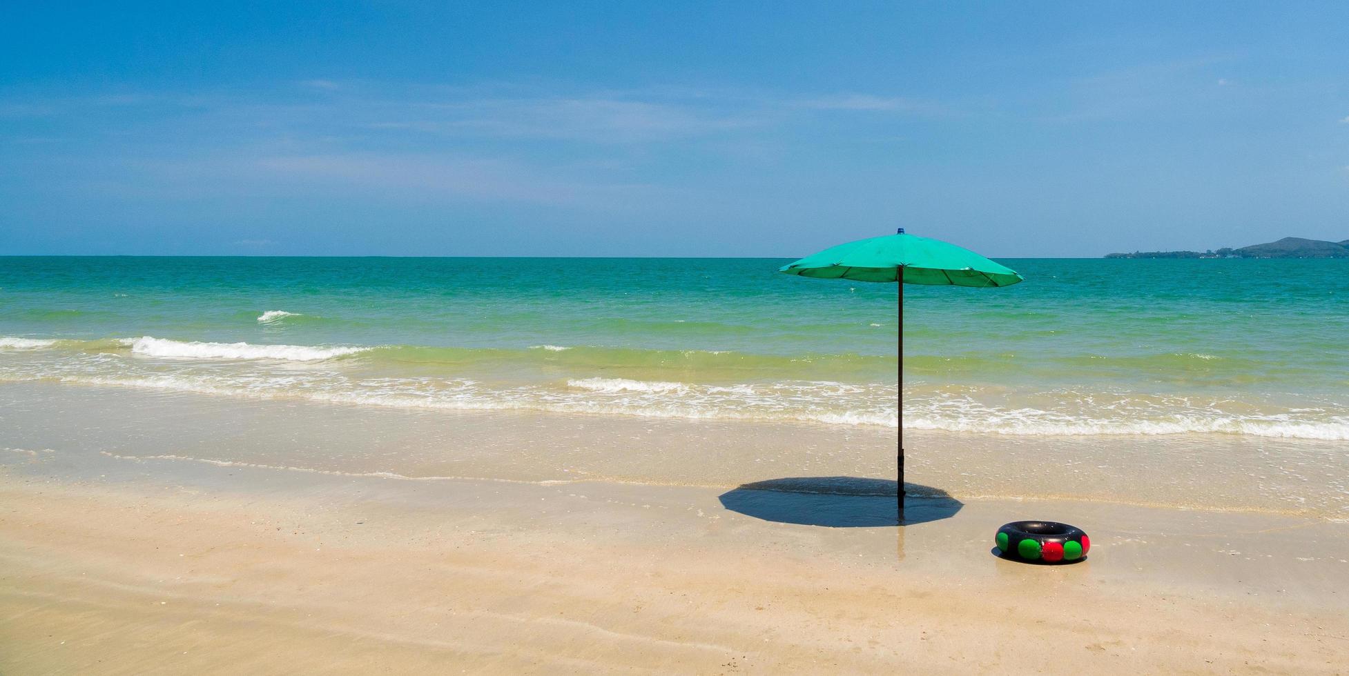 vista frontal del paisaje playa azul ola de mar con cielo fresco de vacaciones con sombrilla verde instalada en la arena para los turistas que indican que no importa cuán caliente sea el sol en verano, la pequeña sombra es valiosa, tailandia foto