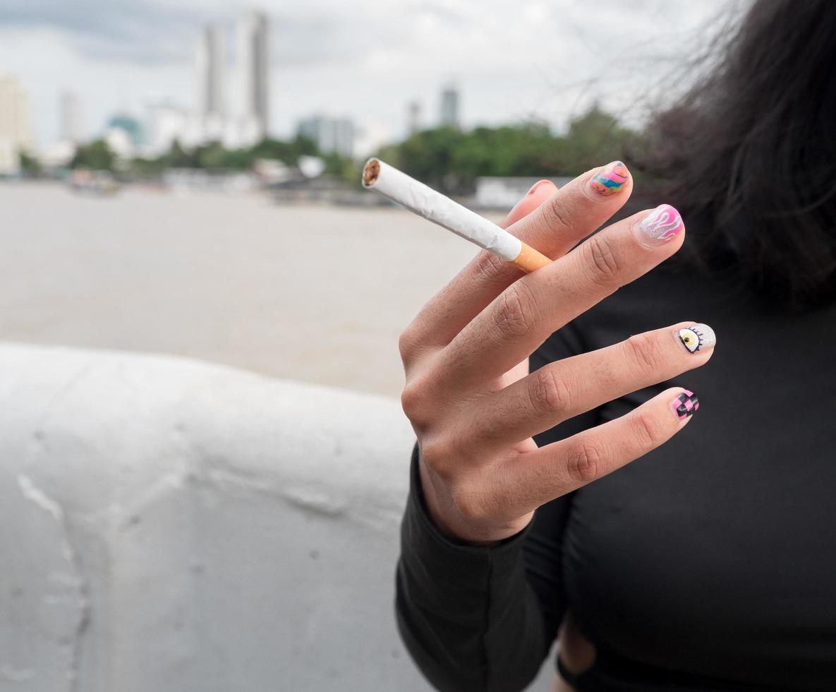 Closeup hand woman teen young asia one person wearing a black shirt hold smoking cigarette white color standing outdoor by the wall photo