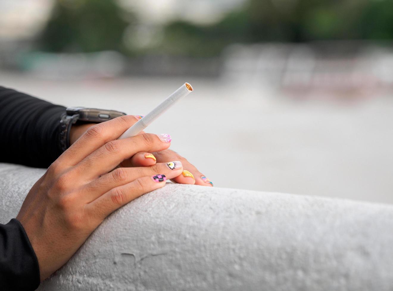 Closeup hand woman teen young asia one person wearing a black shirt hold smoking cigarette white color standing outdoor by the wall photo