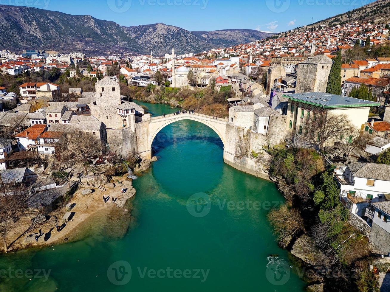 vista aérea de drones del viejo puente en la ciudad de mostar en bosnia y herzegovina durante el día soleado. colores azul turquesa del río neretva. UNESCO sitio de Patrimonio Mundial. gente caminando por el puente. foto