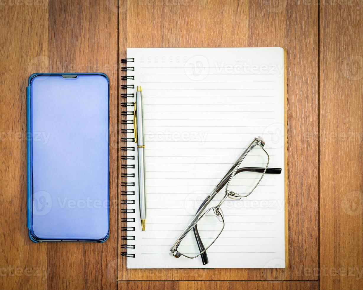 Top view image of open notebook with blank page and cellphone on wooden table photo