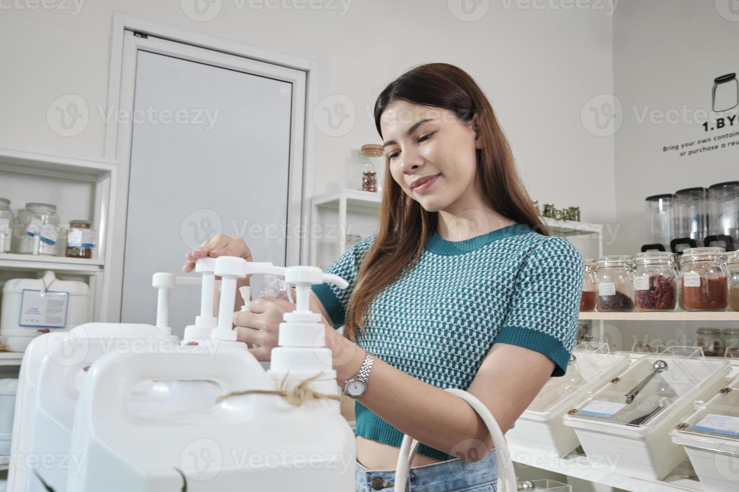 A Caucasian female customer pressed a reusable container to fill liquid products to recycle bottles at zero-waste and refill store, environment-friendly groceries, and sustainable shopping lifestyle. photo