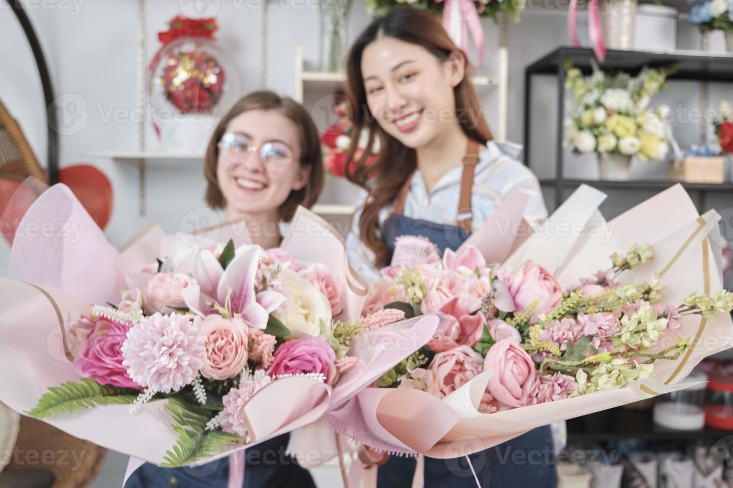 Two young beautiful women florist partners giving floral bunch with a smile, selective focus on a blossom bouquet, lovely business entrepreneur, flower shop happy work, brightly colorful flora store. photo