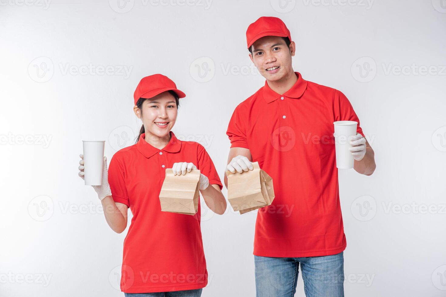 imagen de un joven repartidor feliz con gorra roja en blanco camiseta uniforme mascarilla guantes de pie con un paquete de papel artesanal marrón vacío aislado en un estudio de fondo gris claro foto