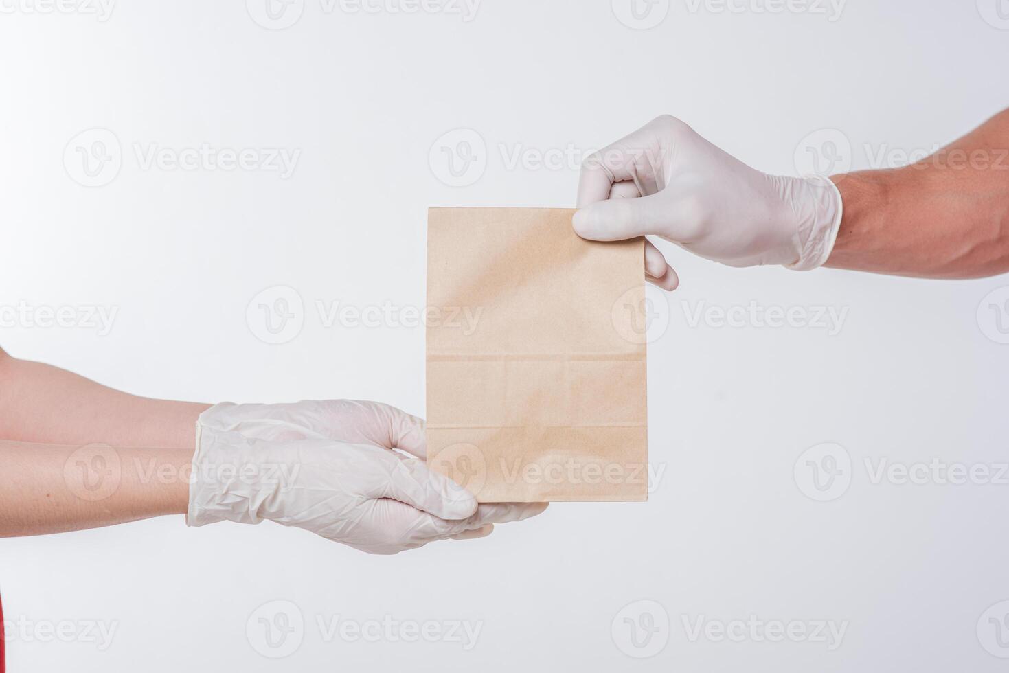 Image of a delivery man in standing with blank brown craft paper packet isolated on light gray background studio photo