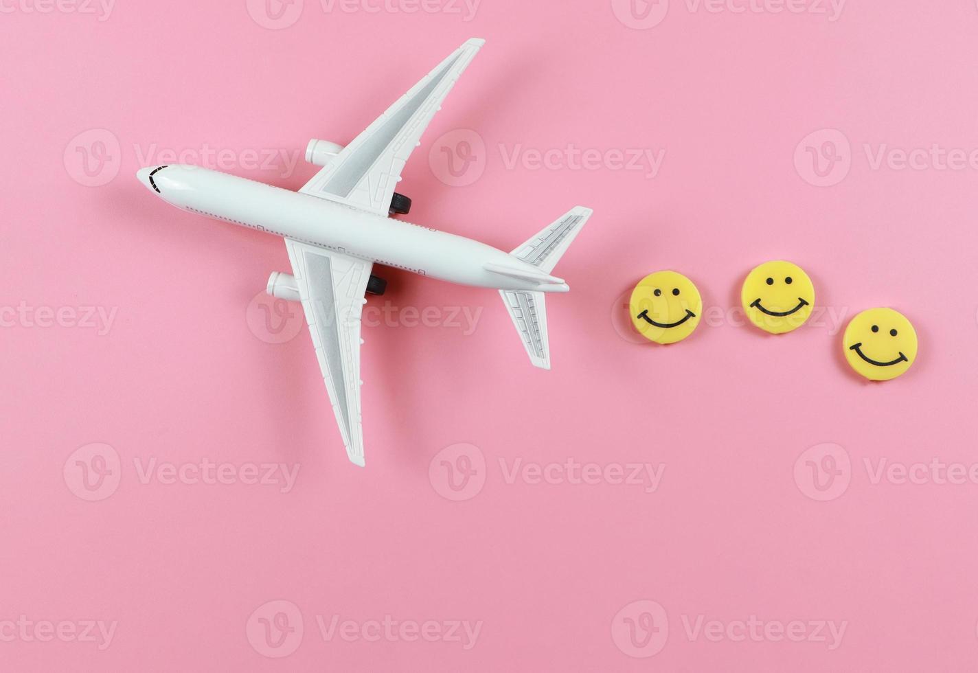 flat lay of airplane model with three yellow circle smiling faces  on pink  background. Happy or fun trip concept. photo
