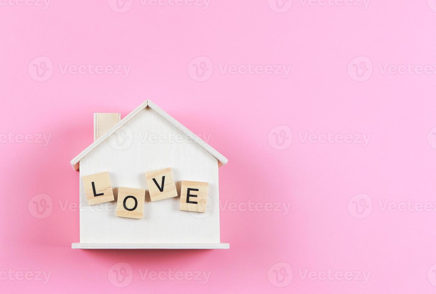 flat lay of wooden model house with wooden letters L O V E on it  on pink  background. dream house , home of love, strong relationship, valentines. photo