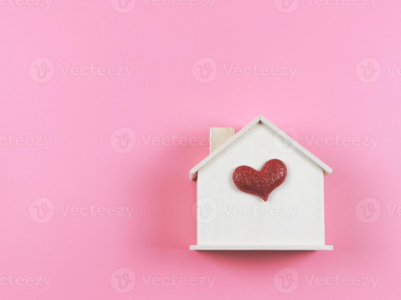 flat lay of wooden model house with red glitter heart on pink  background. dream house , home of love, strong relationship, valentines. photo