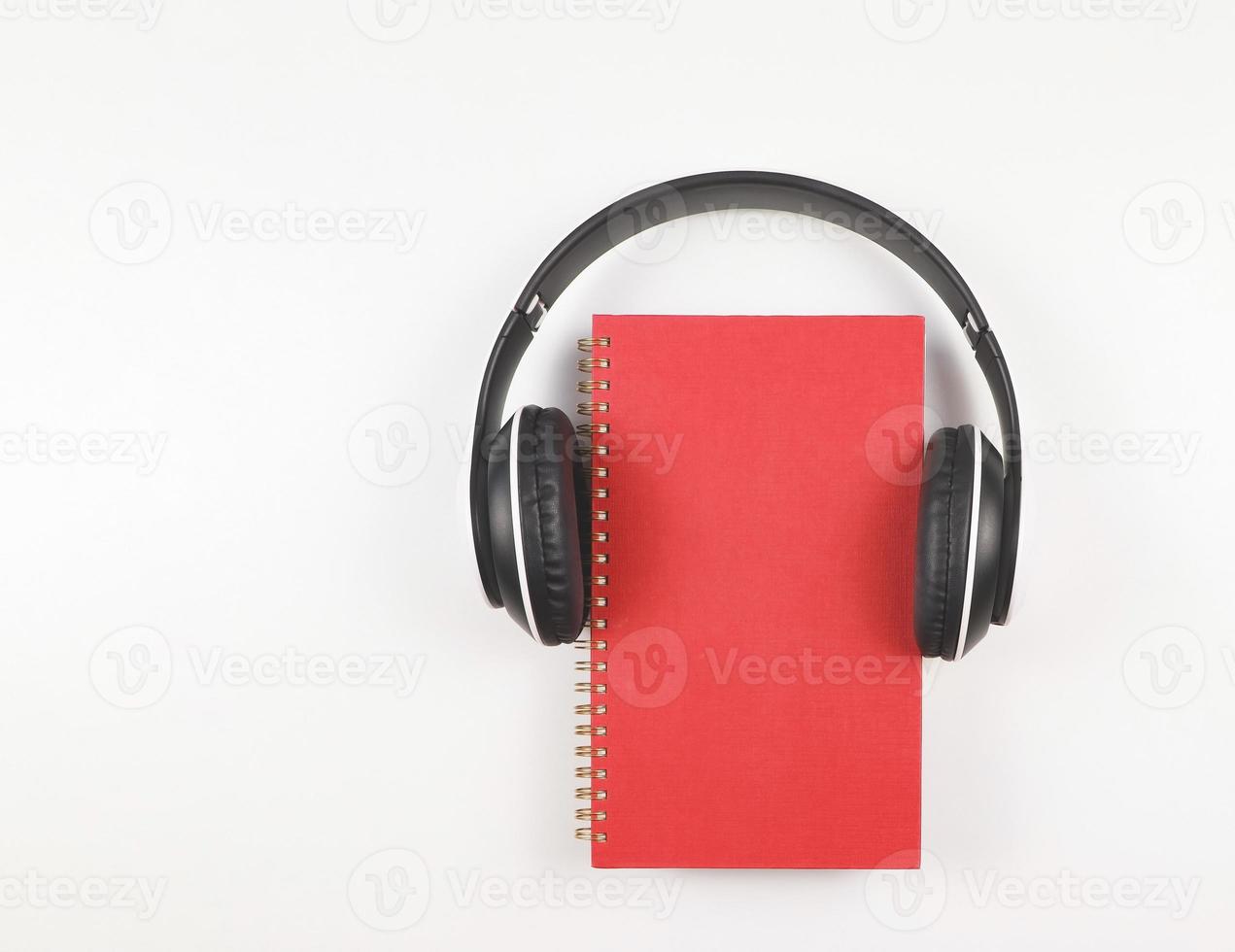 flat lay of red notebook or  diary or planner covered with headphones isolated on white background with copy space.  Audio book or podcast concept. photo