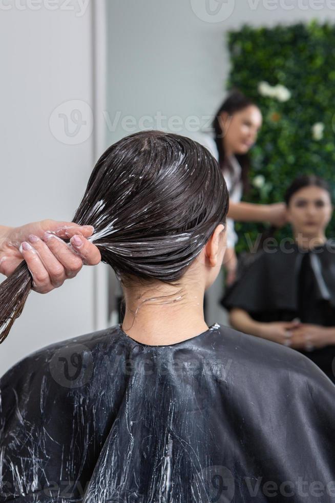 Hairdresser applies a hair mask to straight black hair. Hair care at the beauty salon. photo